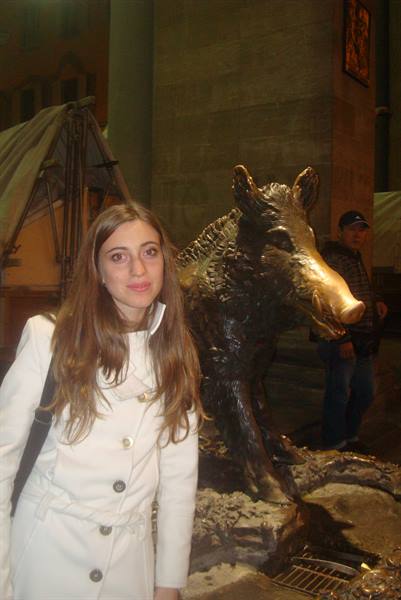 Girl in white coat beside the bronze boar statue of the Porcellino
