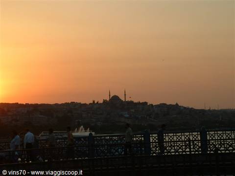People walk on Galata Bridge as Istanbul's mosques glow at sunset
