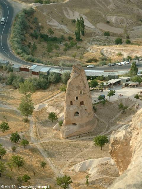 Rock-carved cave dwelling in Göreme, winding road and trees below