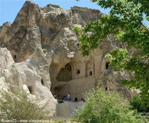 Rock-cut churches in Göreme's volcanic stone, visitors resting under green trees