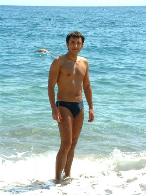 Young man in blue swim trunks standing in the shore waves