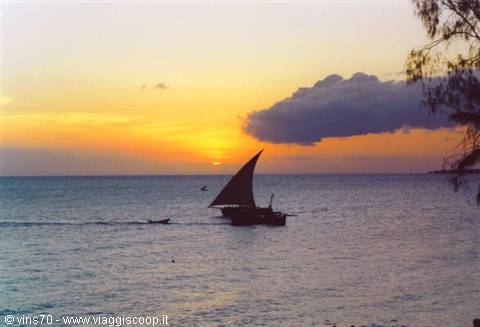 Dhow with triangular sail crossing the sea at sunrise, orange sky and dark clouds