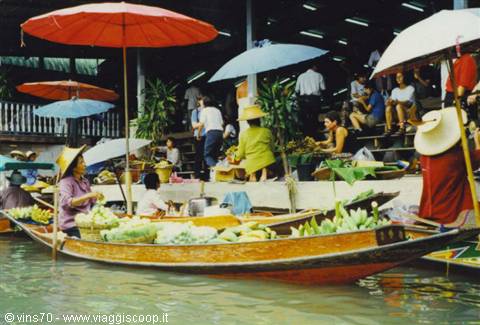 Floating market: women on wooden boats sell fruit and vegetables under colorful umbrellas