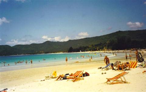 Sunbathers on wooden loungers, white sand, turquoise water, green hills