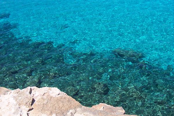 Pale rock over clear turquoise water, dark seabed visible below