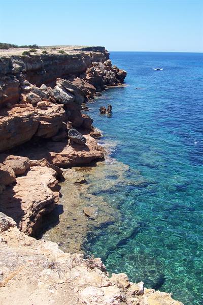 Red cliffs above turquoise clear water under a blue sky