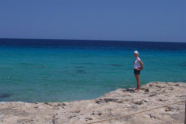 Woman in white hat on limestone rocks, turquoise sea under blue sky