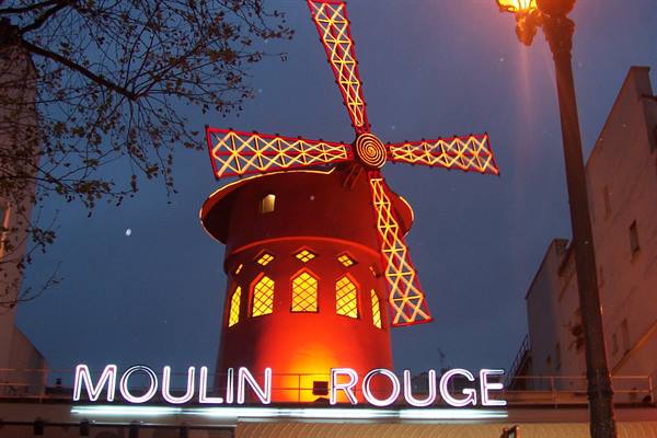 The red neon windmill of the Moulin Rouge in Paris glows at dusk