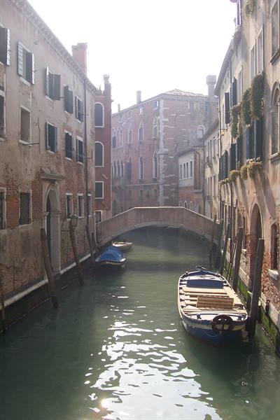 Venice canal with moored boats and a small stone bridge