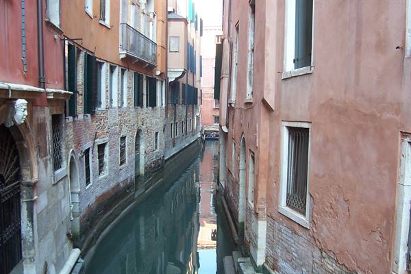 Narrow canal between red Venetian houses, reflections in still water