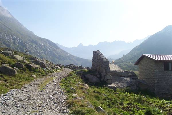 Dirt trail among boulders and old stone wall ruins, stone hut, mountains