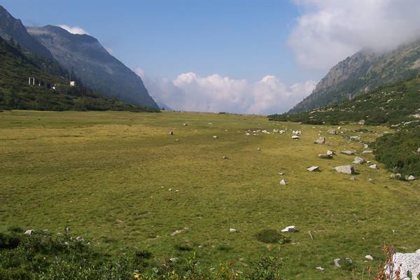 Grassy meadow with granite boulders between mountains, mist on peaks, Val Masino