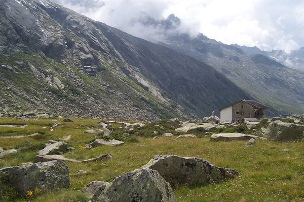 Stone mountain hut amid boulders and meadow, peaks veiled by clouds