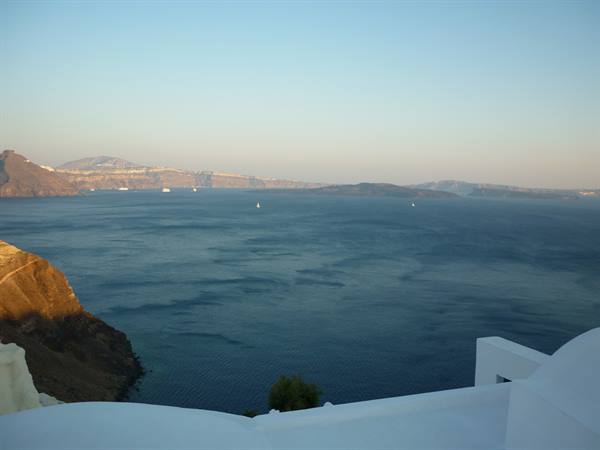 White terrace over the Santorini caldera, a lone sailboat on the blue sea