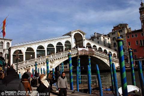 Rialto Bridge in Venice, tourists by the water with striped mooring poles