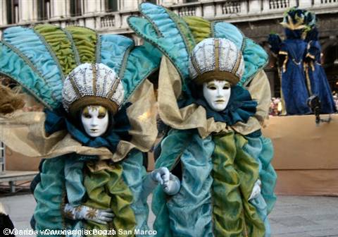 Two costumed figures in blue and green with white masks at St Mark's Square, Venice