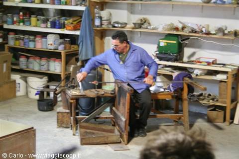 Glassblower shapes molten glass with long blowpipe in his workshop