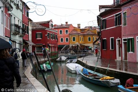 Tourists in the rain along a Burano canal among colorful houses and boats