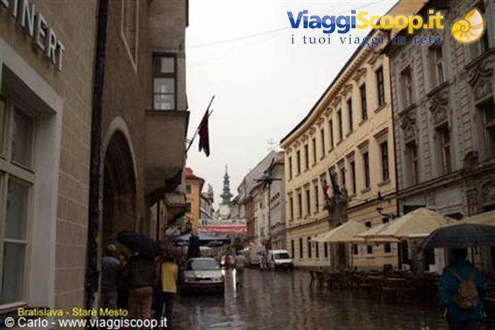 Rain-soaked street with umbrellas and historic buildings in Bratislava