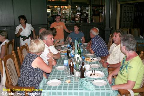 Tourists seated at dinner table with bottles and plates, hotel bar in background