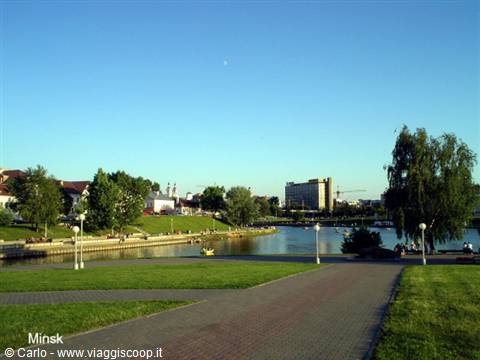 Minsk riverside promenade with paved paths, green lawn and boats on the river