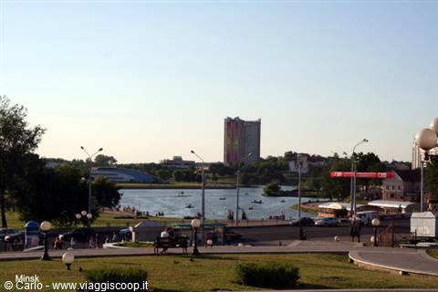 Minsk, Svislach river with people boating, buildings and lampposts under blue sky