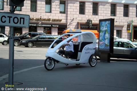 White velotaxi pedaling along the street next to a Stop sign in Moscow