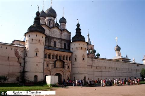 Tourists visit Rostov Kremlin, white walls and onion domes under blue sky