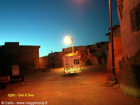 Camper van parked at night among mud-brick houses in Siwa Oasis