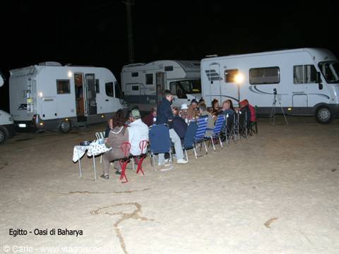 Night dinner among parked campervans on sand with folding chairs, Baharya Oasis