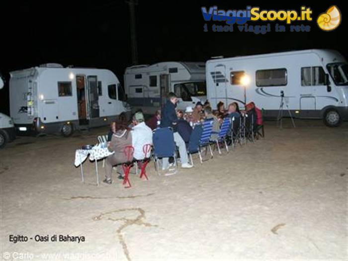 Night dinner among parked campervans on sand with folding chairs, Baharya Oasis