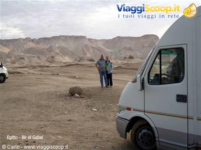 Couple standing beside their camper van near rocky desert mountains at Bir el Gabal