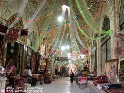 Shiraz bazaar: brick vault with hanging green fabrics, carpets and visitors