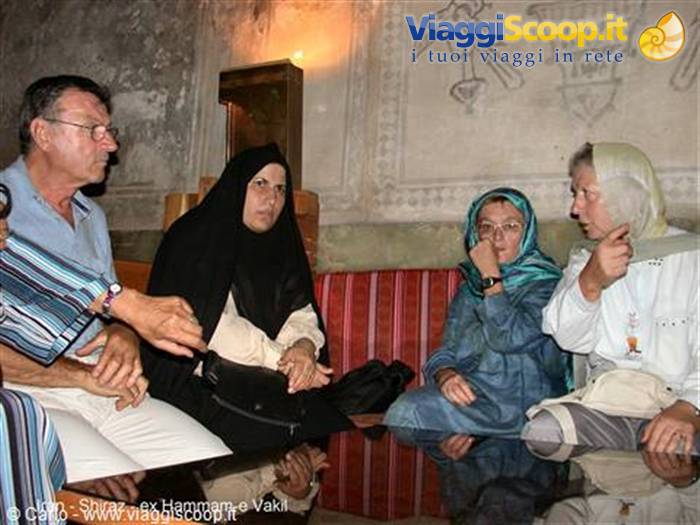 Visitors seated on sofas inside Shiraz's old Vakil bathhouse, murals behind