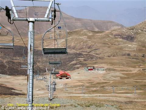 Empty chairlift over arid hills, red cabins at the mountain base, Tehran
