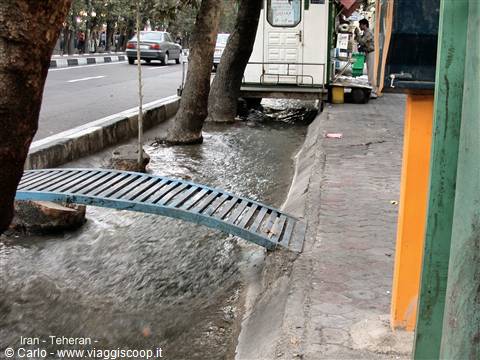 Tehran: small blue metal bridge over a water channel beside the sidewalk