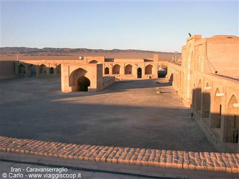 Brick caravanserai in the desert, arched porches lit by morning sun