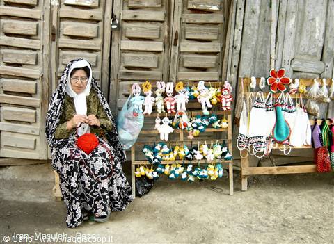 Veiled craftswoman knits wool dolls before wooden doors in Masuleh