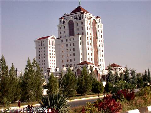 White building with red roofs in Ashgabat, among pines and flowers