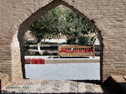 Brick arch in Khiva with wooden daybed and red carpets in the shade
