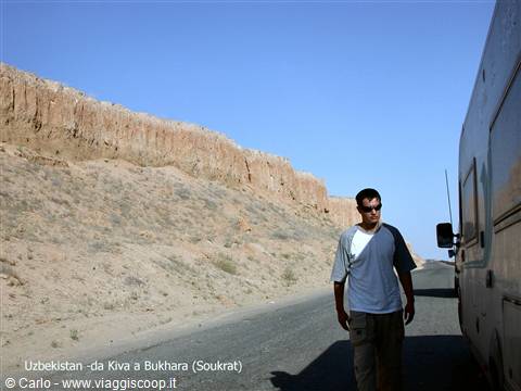 Man beside camper on the road between Khiva and Bukhara, red rock cliffs