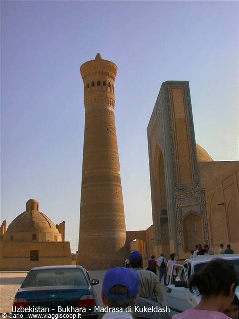 Brick minaret in Bukhara, decorated portal, tourists and cars below