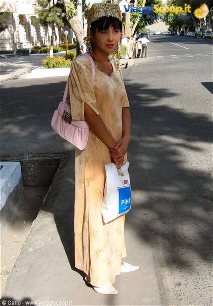 Woman in golden dress and traditional headdress on a Tashkent sidewalk