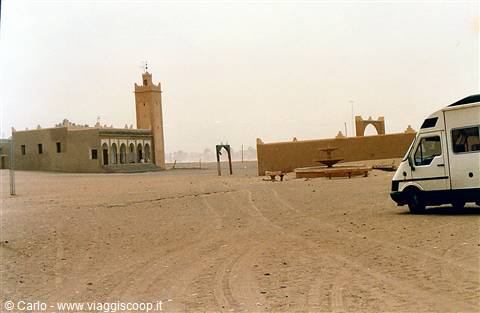 Mud-brick mosque with minaret, camper van parked on the sand