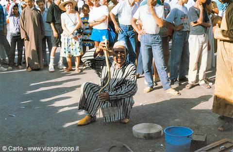 Snake charmer in striped robe sitting on the ground among the crowd, Marrakech