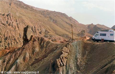 White motorhome on dirt road among eroded rocky hills