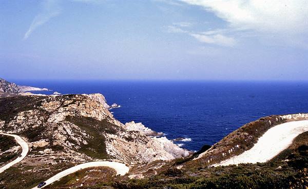 Dirt road winding over granite rocks above deep blue sea
