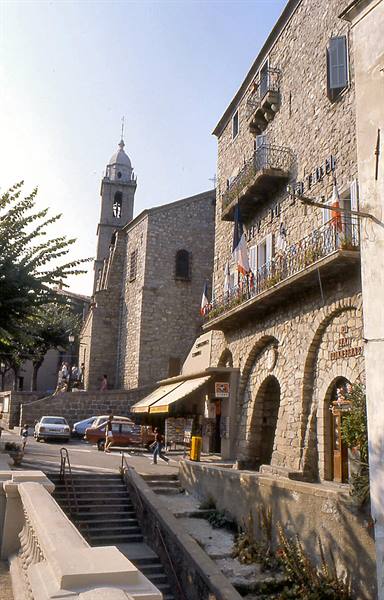 Stone church with bell tower and French flag balconies in a Corsican village