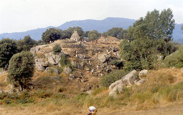 Stone ruins on a rocky hill, tourists climbing among Mediterranean scrub and mountains