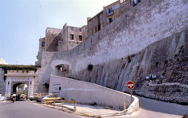 Old stone walls above the road, vintage cars and an arched gateway